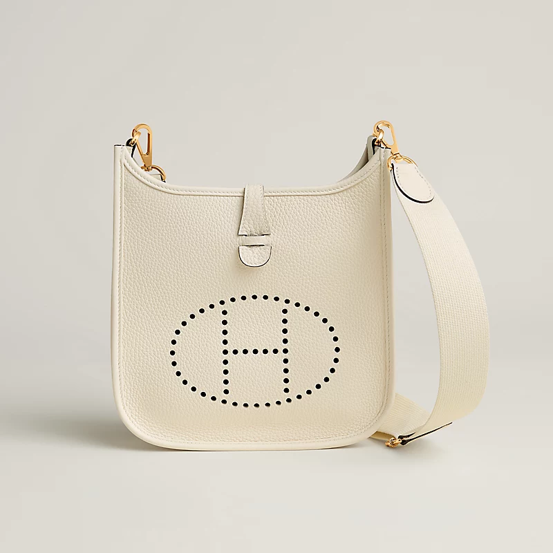 Cream leather handbag with perforated oval 'H' logo and wide detachable shoulder strap with gold hardware.